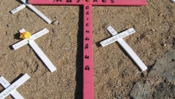 Ein pinkfarbenes Kreuz mit der Aufschrift „Mujeres Chihuahua“ inmitten vieler weißer Kreuze auf dem Boden.