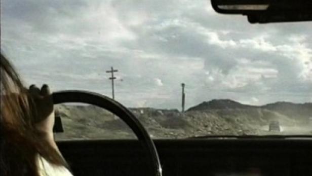 Eine Person fährt durch eine trockene Landschaft mit bewölktem Himmel.