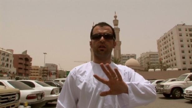 Ein Mann in traditioneller Kleidung steht vor einer Moschee und einem Parkplatz.