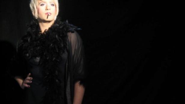 Eine Frau mit Federboa und Zigarettenspitze posiert im Scheinwerferlicht.