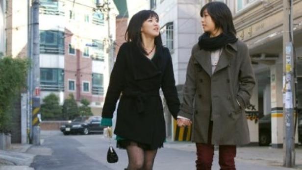 Zwei junge Frauen gehen Händchen haltend eine Straße entlang.