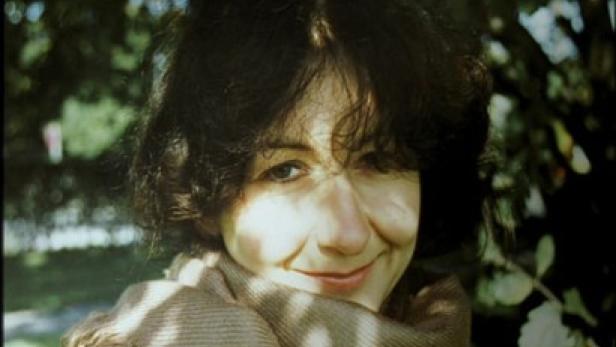 Eine lächelnde Frau mit dunklen Haaren und einem Schal im Freien.