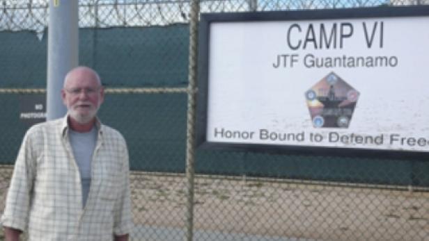 Ein Mann steht vor einem Schild mit der Aufschrift „Camp VI JTF Guantanamo“.