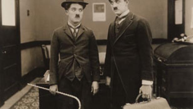 Charlie Chaplin und ein weiterer Mann, beide mit Melone und Schnurrbart, stehen nebeneinander.