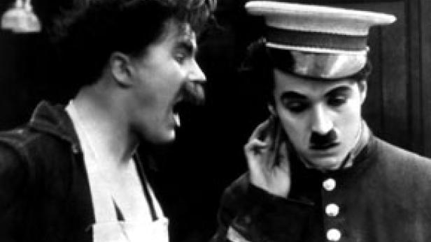 Charlie Chaplin als Soldat mit einem schreienden Mann im Hintergrund.