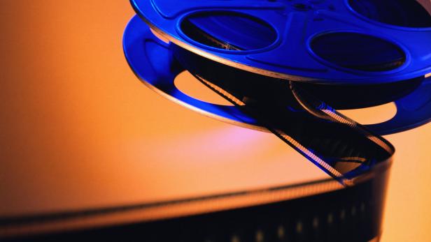 Eine blaue Filmrolle mit einem aufgewickelten Filmband vor einem orangefarbenen Hintergrund.