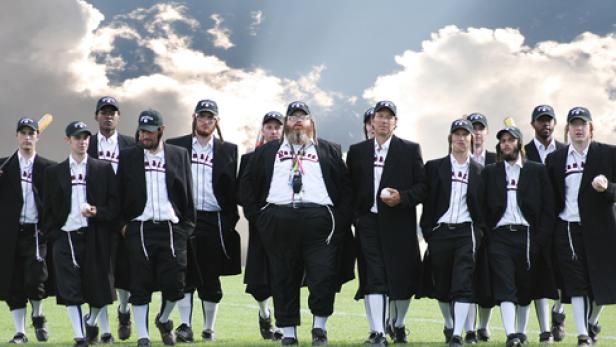 Eine Gruppe von Männern in Baseballuniformen und schwarzen Mänteln steht auf einem Feld.