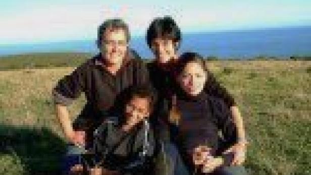 Eine Gruppe von vier Personen sitzt auf einer Wiese mit Blick auf das Meer.