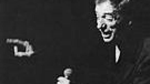 Ein Mann in einem dunklen Anzug gestikuliert und spricht in ein Mikrofon.