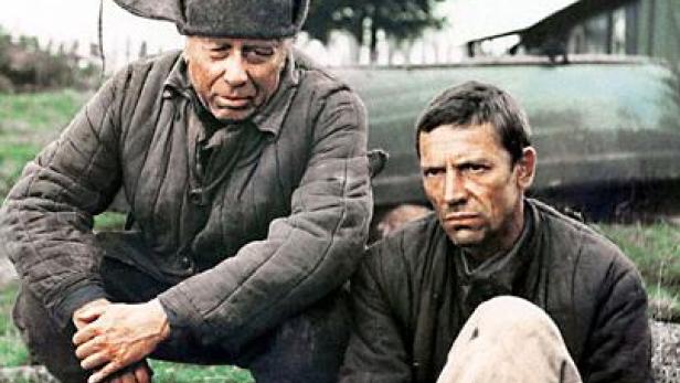 Zwei Männer in Arbeitskleidung sitzen im Freien.