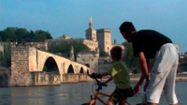 Ein Vater lehrt seinem Sohn das Fahrradfahren vor der Brücke von Avignon.