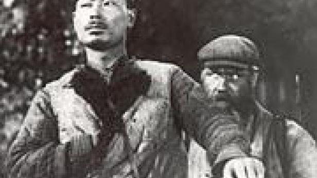 Ein Mann mit Mütze und ein Mann mit Bart stehen nebeneinander.