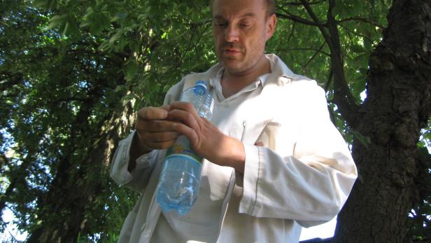 Ein Mann im weißen Kittel betrachtet eine Plastikwasserflasche unter einem Baum.