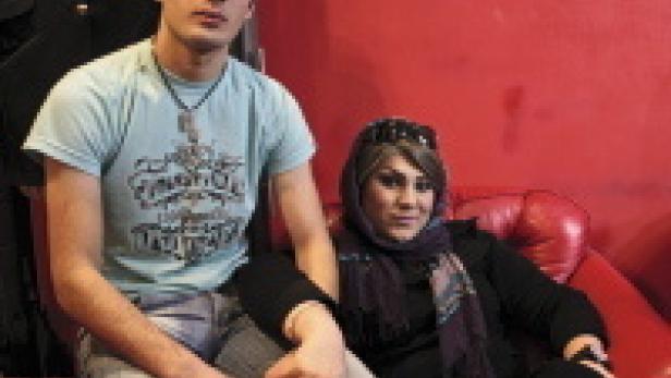 Ein junger Mann und eine Frau sitzen auf einem roten Sofa vor einer roten Wand.