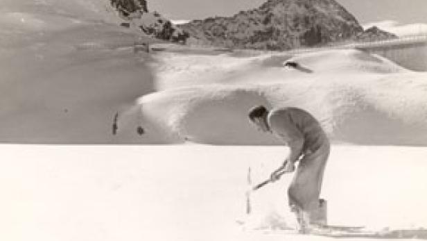 Ein Mann hackt mit einer Spitzhacke in einer verschneiten Landschaft.
