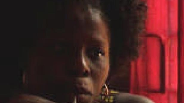 Eine Frau mit dunkler Haut und lockigem Haar vor einem roten Hintergrund.