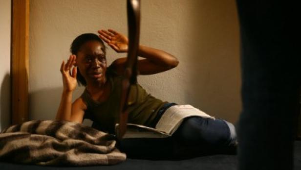 Eine verängstigte Frau liegt mit einem Buch auf einem Bett und hält die Hände schützend vor das Gesicht.