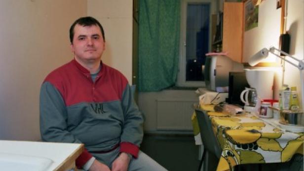 Ein Mann sitzt in einem Zimmer mit Schreibtisch und einem kleinen Fernseher.