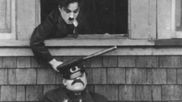 Charlie Chaplin zielt mit einem Gewehr auf einen schlafenden Polizisten.