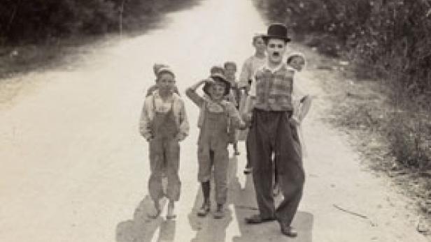 Charlie Chaplin geht mit einer Gruppe von Kindern auf einer Landstraße.