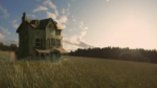 Ein verlassenes, grünes Haus steht auf einem Feld unter blauem Himmel.