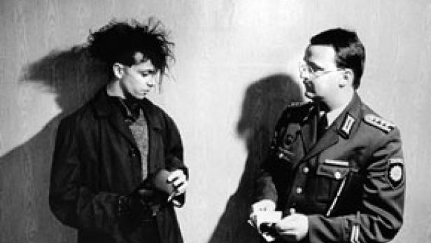 Ein junger Mann mit auffälliger Frisur wird von einem Polizisten kontrolliert.