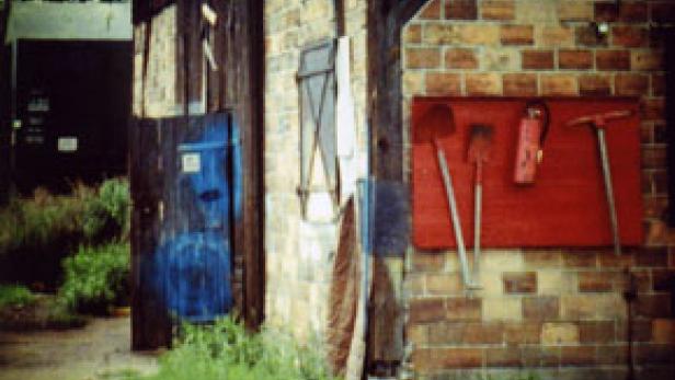 Eine rote Tafel an einer Backsteinmauer mit Schaufeln, einem Feuerlöscher und einer Spitzhacke.