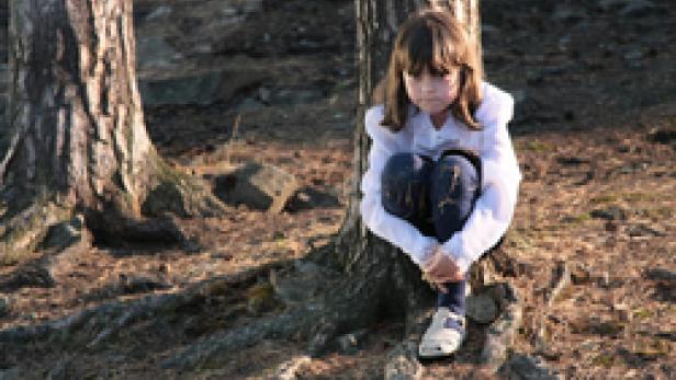 Ein trauriges Mädchen sitzt an einem Baum im Wald.