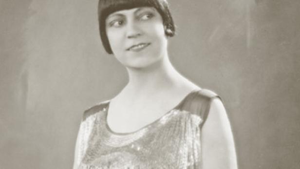 Eine Frau mit Bubikopf und Paillettenkleid lächelt zur Seite.