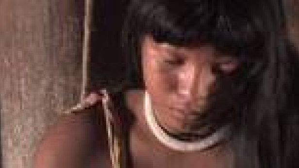 Eine indigene Frau mit dunklen Haaren und einem weißen Halsband blickt nach unten.