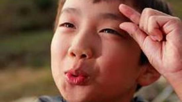 Ein Junge formt mit seinen Fingern eine kleine Geste vor seiner Stirn.