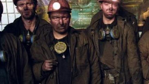 Eine Gruppe von Bergleuten mit schmutzigen Gesichtern und Helmen steht zusammen.