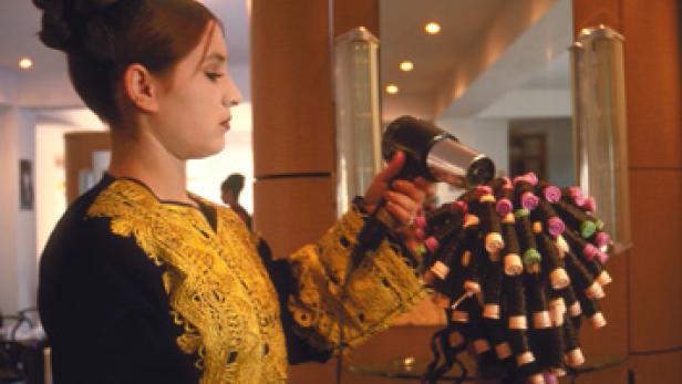 Eine Frau mit traditioneller Kleidung föhnt die Haare einer anderen Frau mit Lockenwicklern.