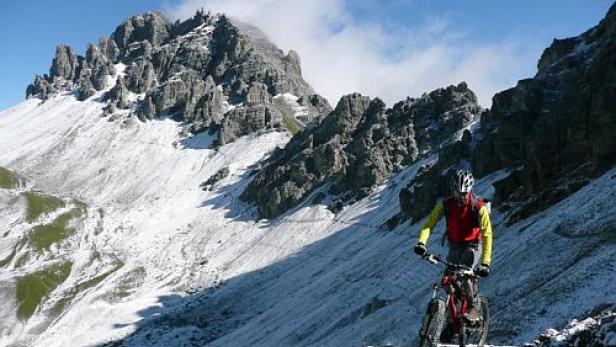 Ein Mountainbiker fährt auf einem Pfad in den verschneiten Bergen.