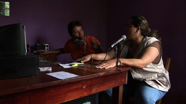 Zwei Frauen sitzen an einem Tisch mit Mikrofonen und sprechen.