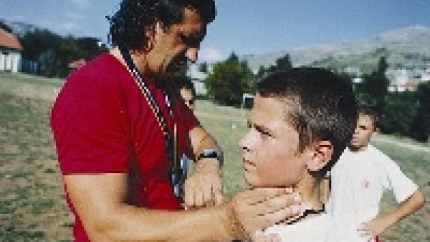 Ein Mann untersucht den Hals eines Jungen im Freien.