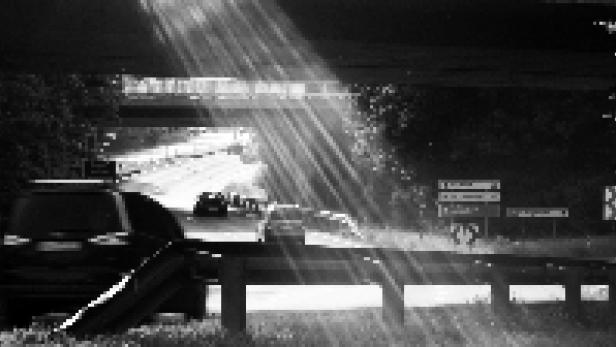 Sonnenstrahlen scheinen unter einer Autobahnbrücke auf eine Straße mit Autos.