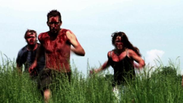 Mehrere blutverschmierte Menschen rennen durch hohes Gras.