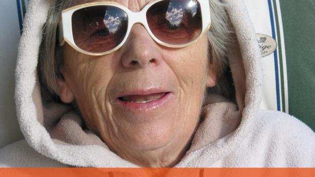 Eine ältere Frau mit Sonnenbrille und Kapuzenpullover liegt entspannt im Liegestuhl.