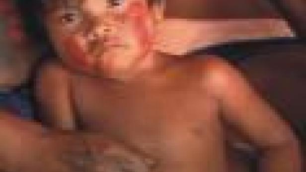 Ein indigenes Kind mit roter Farbe im Gesicht sitzt auf dem Schoß einer Person.