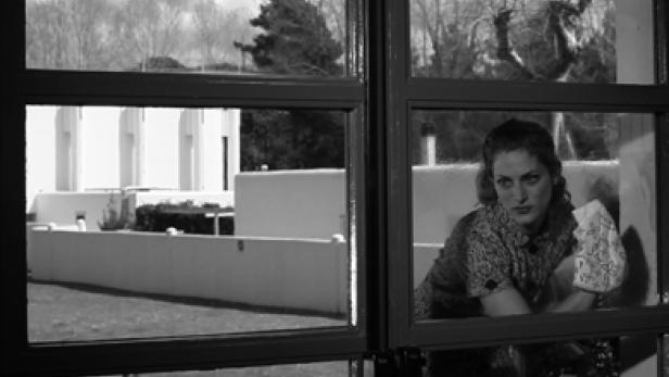 Eine Frau mit einem Tuch in der Hand schaut aus dem Fenster.