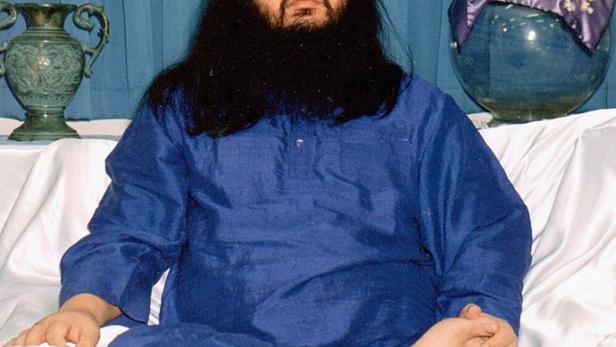 Ein Mann mit langem, dunklem Haar und Bart sitzt in Meditationshaltung.