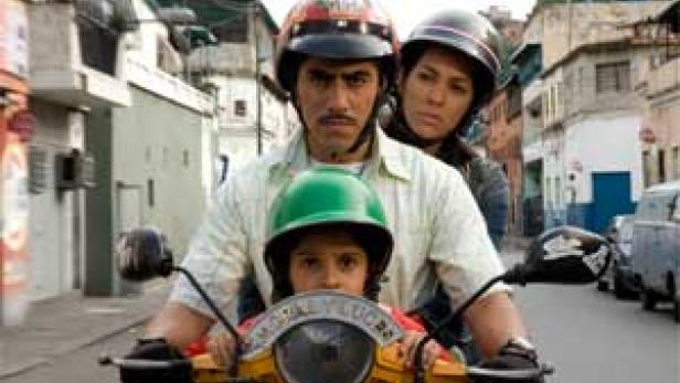 Ein Mann fährt mit einem Motorroller und transportiert ein Kind und eine Frau, alle mit Helmen.