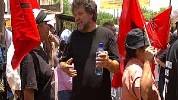 Eine Menschenmenge mit roten Fahnen demonstriert auf einer Straße.