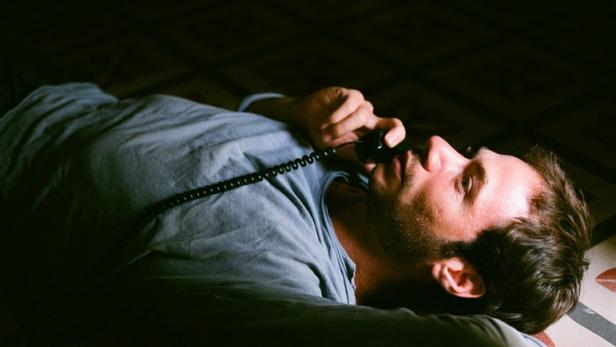 Ein Mann liegt auf dem Boden und telefoniert mit einem alten Telefon.