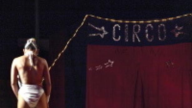 Eine Frau in einem weißen Badeanzug steht vor einem Zirkuszelt.