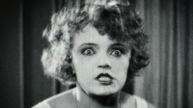 Eine Frau mit lockigem Haar blickt mit aufgerissenen Augen in die Kamera.