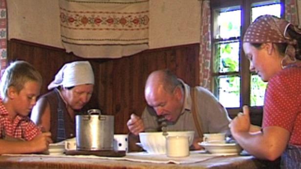 Eine Familie sitzt an einem Holztisch und isst gemeinsam eine Mahlzeit.