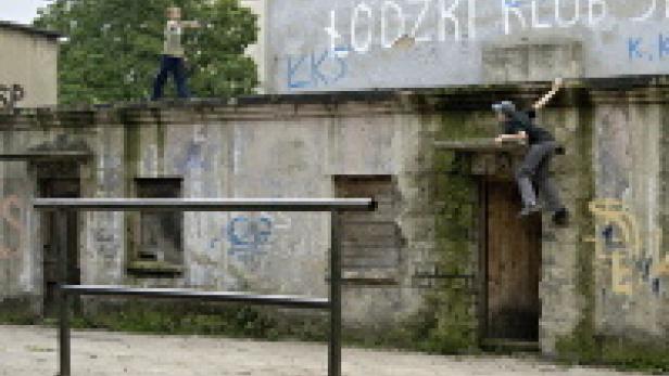 Zwei Personen üben Parkour an einer Mauer mit Graffiti.