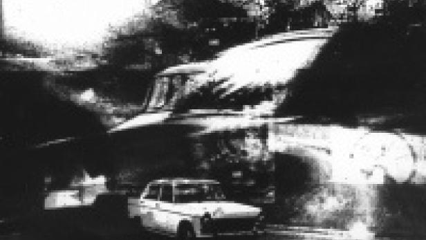 Ein weißes Auto fährt auf einer kurvenreichen Straße an einem Haus vorbei.